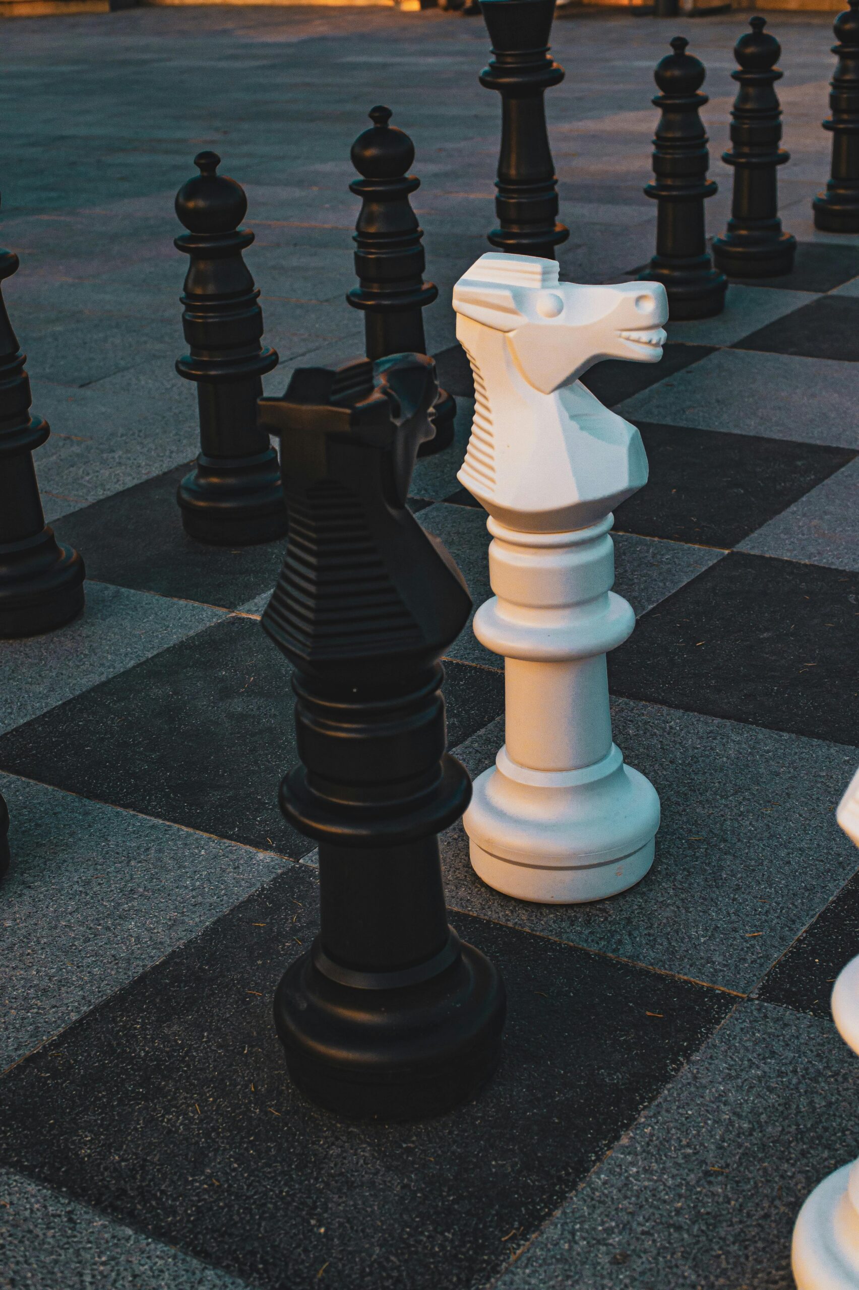 Outdoor chess game with large black and white pieces on a checkered board.