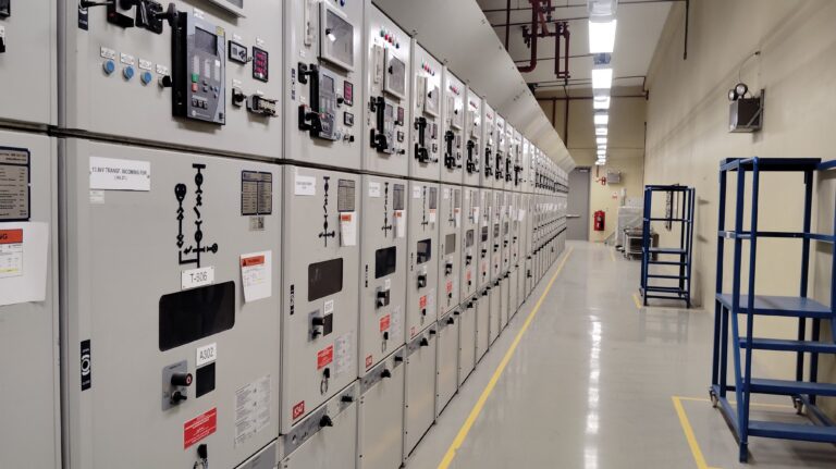 Long row of control panels in an industrial electrical control room, well-lit and spacious.