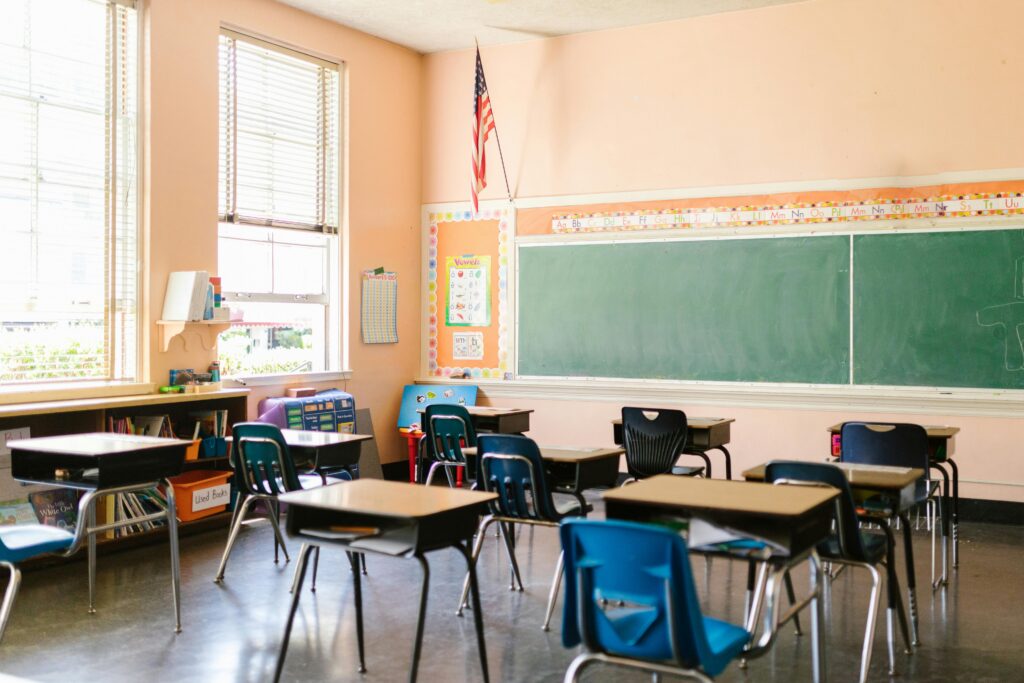 An inviting, sunlit classroom with empty desks and an American flag, ready for students.