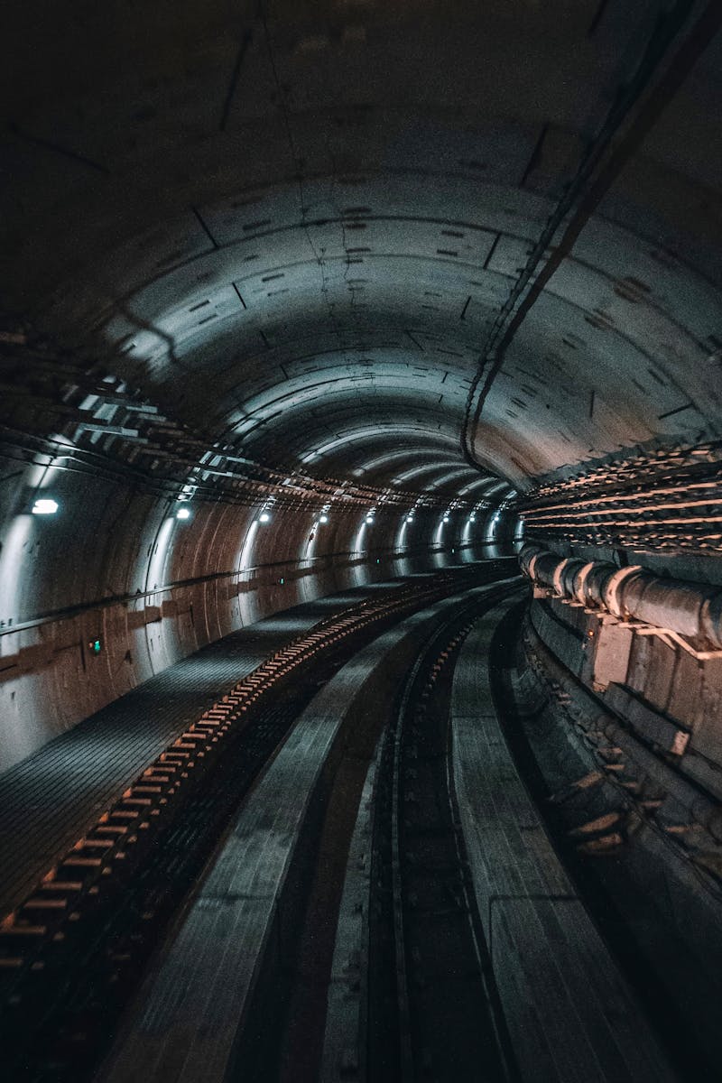 A dimly lit underground subway tunnel showcasing curving tracks and utility pipes.